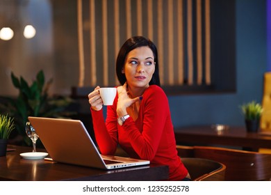 Beautiful young woman holding coffee in a cafe with a laptop on the table - Shutterstock ID 1235252578