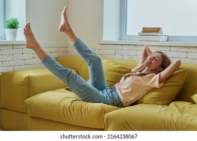 Beautiful young woman holding hands behind head and smiling while relaxing on the couch at home