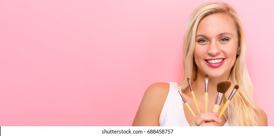 Beautiful Young Woman Holding Makeup Brushes On A Pink Background