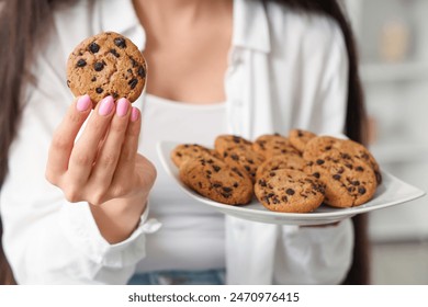 Beautiful young woman holding plate of tasty cookies with chocolate chips at home, closeup - Powered by Shutterstock