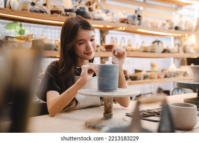 Beautiful young woman holding pottery instrument for scraping, smoothing, shaping and sculpting. Lady siting on bench with pottery wheel and making clay pot - Powered by Shutterstock