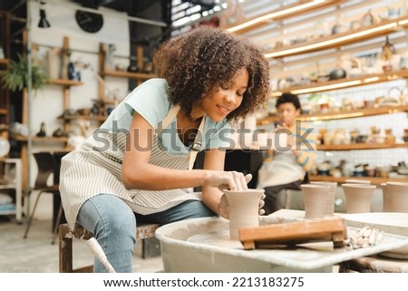 Beautiful young woman holding pottery instrument for scraping, smoothing, shaping and sculpting. Lady siting on bench with pottery wheel and making clay pot