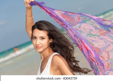 Beautiful young woman holding a purple shawl against the ocean breeze enjoying the South Beach shoreline in Miami.