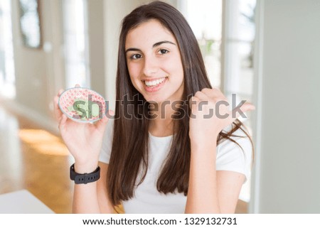 Beautiful young woman holding spicy asian wasabi pointing and showing with thumb up to the side with happy face smiling