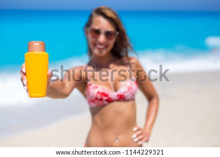 Beautiful young woman holding sunscreen into the camera while smiling
