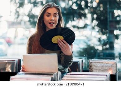 Beautiful young woman holding vinyl while browsing records in a record store. Audiophile and music lover. Vintage Vinyl LP In Records Shop.