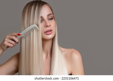 beautiful young woman holds a comb in her hands. Blonde woman with long straight hair on a gray background - Shutterstock ID 2231106471