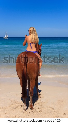 Beautiful young woman horse riding on a tropical beach