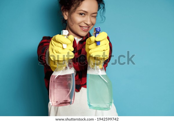 Beautiful young woman, housewife directs cleaning
sprays as if shooting from a pistol, smiling maliciously and
covering one eye at the camera. Focus on hands in gloves holding
sprays. Copy space