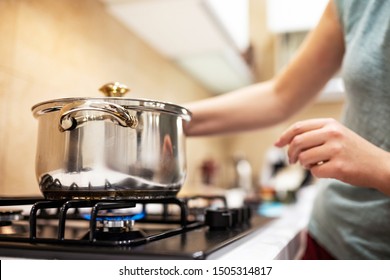 Красивая молодая домохозяйка готовит ужин, держит в руках большую стальную кастрюлю, стоя ее на газовой плите.