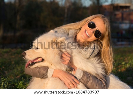 Beautiful young woman hugging her cute samoyed dog in the park at sunset 