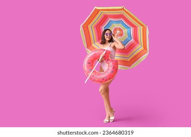 Beautiful young woman with inflatable ring and umbrella on purple background - Powered by Shutterstock