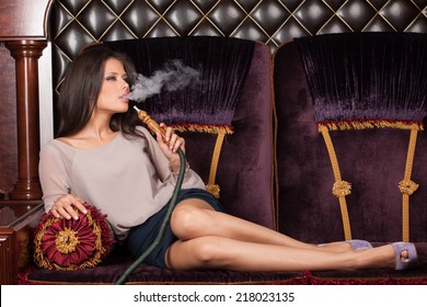 Beautiful Young Woman Inhaling Hookah. Girl Smoking Shisha Lying On Sofa In Cafe