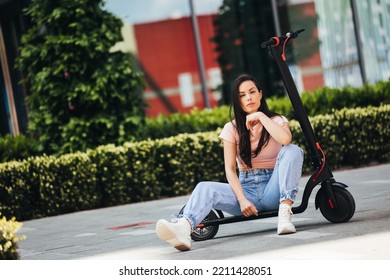 Beautiful Young Woman In Jeans Is Sitting On Her Electro Scooter On The Street