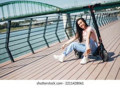 Beautiful Young Woman In Jeans Is Sitting On Her Electro Scooter On The Street