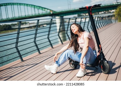 Beautiful Young Woman In Jeans Is Sitting On Her Electro Scooter On The Street