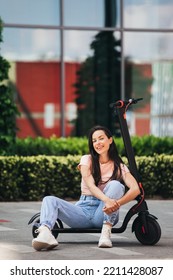 Beautiful Young Woman In Jeans Is Sitting On Her Electro Scooter On The Street