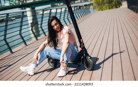 Beautiful Young Woman In Jeans Is Sitting On Her Electro Scooter On The Street