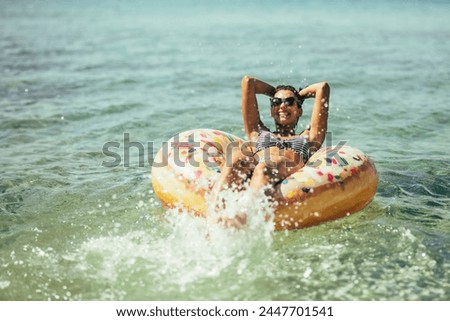 A beautiful young woman is joyfully riding on an inflatable tube as it bobs on the waves in the ocean.