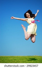 A beautiful young woman jumping in a field with a blue sky.