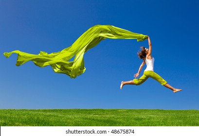 Beautiful young woman jumping on  a green meadow with a colored tissue