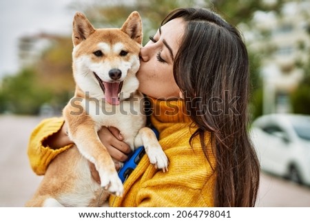 Beautiful young woman kissing and hugging shiba inu dog at street