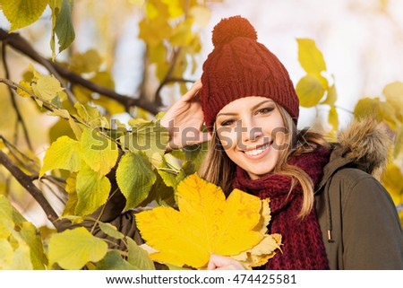 Beautiful Young Woman In Knitted Dark Red Beanie Hat With Pompom And Scarf Outdoors In Park Beautiful Young Woman In Knitted Dark Red Beanie Hat With Pompom And Scarf Outdoors In Park