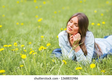 Beautiful young woman laying on grass with dandelion flowers in park