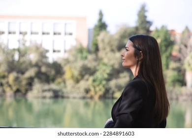 Beautiful young woman leaning over the railing of the river in Seville, Spain. The photo is taken from behind and she is looking at the horizon where you can see the other bank.