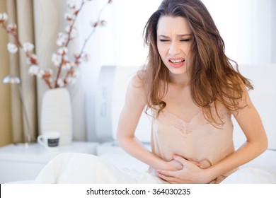 Beautiful Young Woman In Lingerie Sitting On Bed And Suffering From Abdominal Pain 