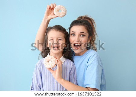 Beautiful young woman and little girl with donuts on color background