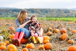 Beautiful Young Woman And Little Kid Daughter, Girl Having Fun With Farming On A Pumpkin Patch. Traditional Family Festival With Children, Thanksgiving And Halloween Concept.