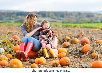 Beautiful young woman and little kid daughter, girl having fun with farming on a pumpkin patch. Traditional family festival with children, thanksgiving and halloween concept.