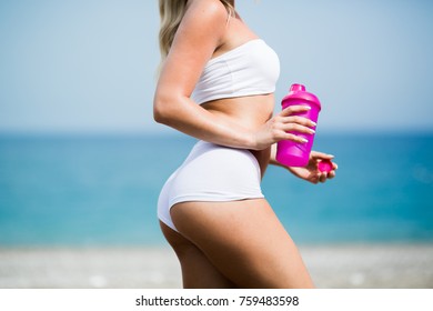 Beautiful young woman with long blond hair in white shorts is standing a back on the coastline of the sea