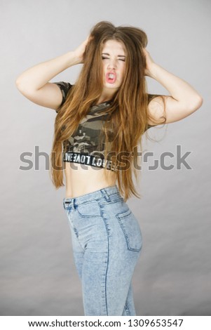 Beautiful young woman with long brown hair wearing stylish camo pattern tshirt and jeans making funny face.