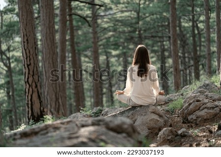 Beautiful young woman with long brunette hair meditates in nature, in a beautiful forest. Travel and healthy lifestyle, enjoying nature