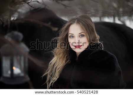 Beautiful young woman in a long dress with a black horse