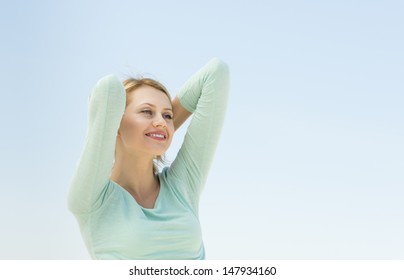 Beautiful young woman looking away with arms raised against clear blue sky