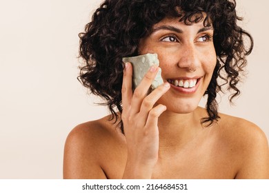 Beautiful Young Woman Looking Away With A Smile While Holding A Bar Of Natural Soap Close To Her Face. Happy Young Woman Using Handmade Cosmetic Soap To Take Care Of Her Skin.