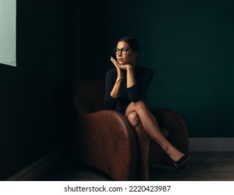 Beautiful Young Woman Looking Away While Sitting On A Chair. Young Asian Female Looking Outside The Window While Sitting In An Office Lobby.