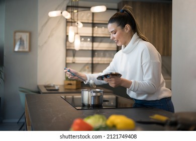 A Beautiful Young Woman Looking At The Soup She Is Cooking. Healthy Life Style.