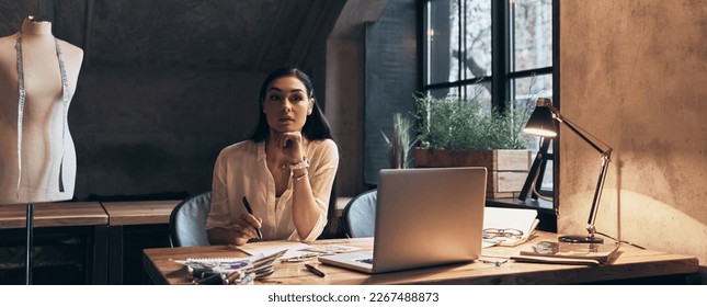 Beautiful young woman looking thoughtful while sitting at her working place in office - Shutterstock ID 2267488873