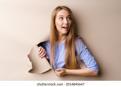 Beautiful young woman looking through a hole in beige paper