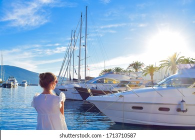 Beautiful young woman looking at the white luxury yachts in the marina during sunset 