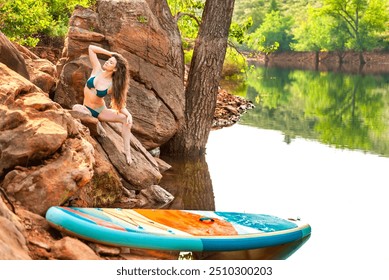 Beautiful young woman lounging on a rock by a mountain lake with a standup paddleboard - Powered by Shutterstock