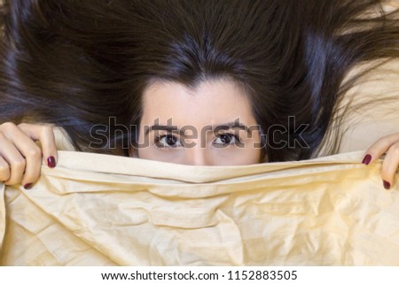 Beautiful young woman lying down in the bed and sleeping. Teen girl with open eyes covers her face with white blanket in the morning. Do not get enough sleep concept. View from above. Copy space.