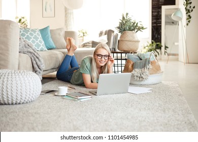 Beautiful young woman lying on the floor in living room at home and using a laptop.