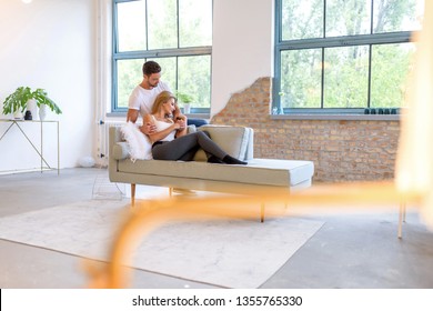 A beautiful young woman lying on the sofa with boyfriend hugging her from behind.