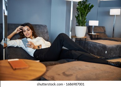 Beautiful young woman lying on comfortable daybed and reading message on smartphone stock photo