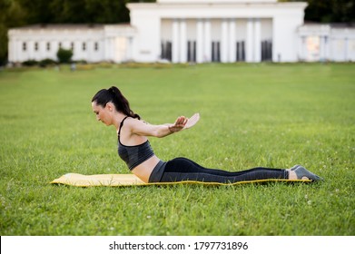 Beautiful young woman lying on a yellow mattress, pose while wearing a tight sports outfit in the park doing pilates or yoga, swan dive expert exercises
